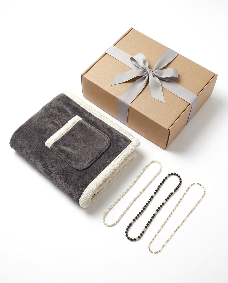 The Evening In set: the folded charcoal wrap with its pocket, three eyeglass chains, and the kraft gift box with a grey ribbon