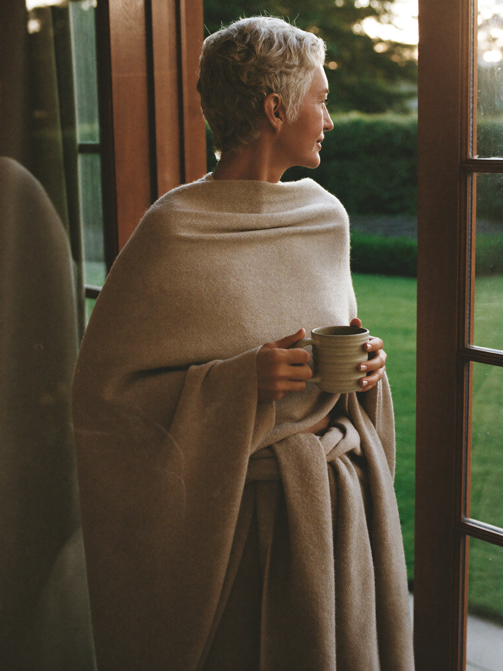 A woman at her front door wrapped in the Evening Wrap, holding a mug
