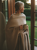A woman at her front door wrapped in the Evening Wrap, holding a mug