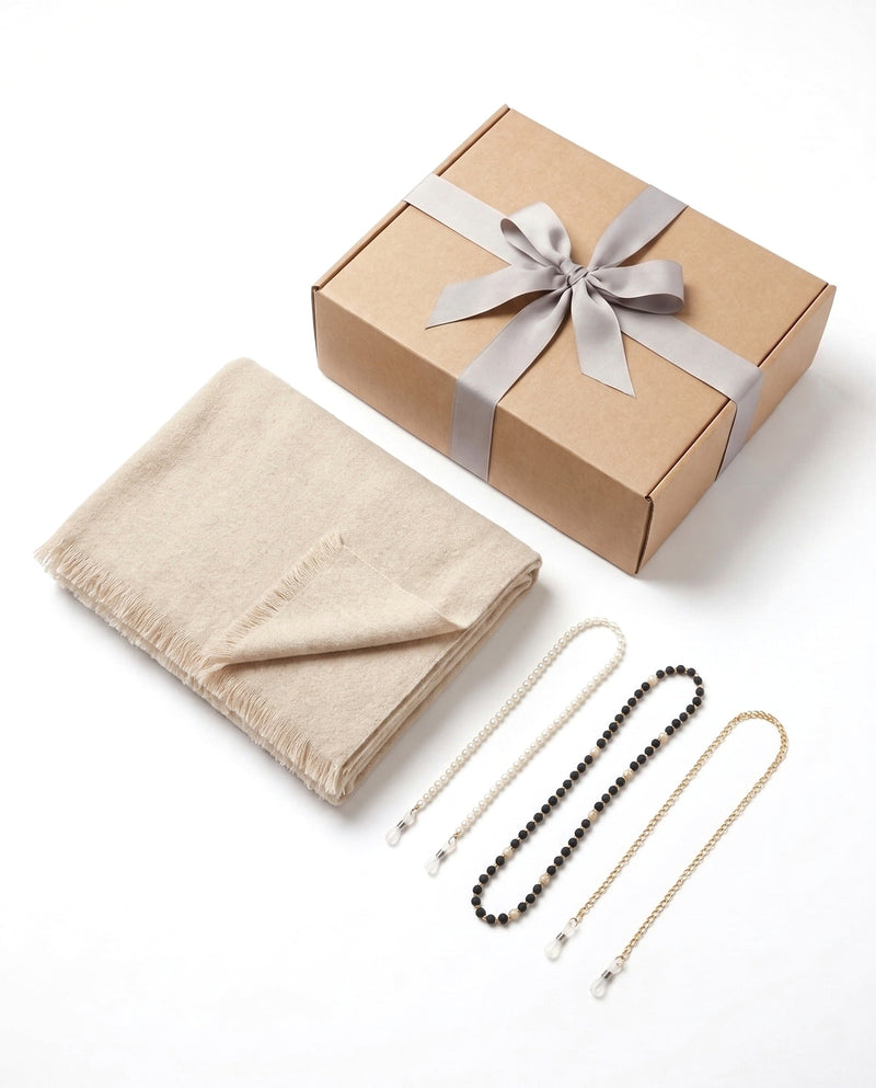 The Long Way Home set: the folded oatmeal beige wrap with its fringed edge, three eyeglass chains, and the kraft gift box with a grey ribbon